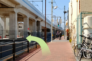 信号を左に渡り、高架線路をくぐります。(交差点から、右には赤い看板のラーメン屋が見えます)