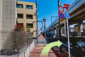 信号を右へ渡り、高架線路をくぐります。(交差点から、左に赤い看板のラーメン屋さんが見えます)